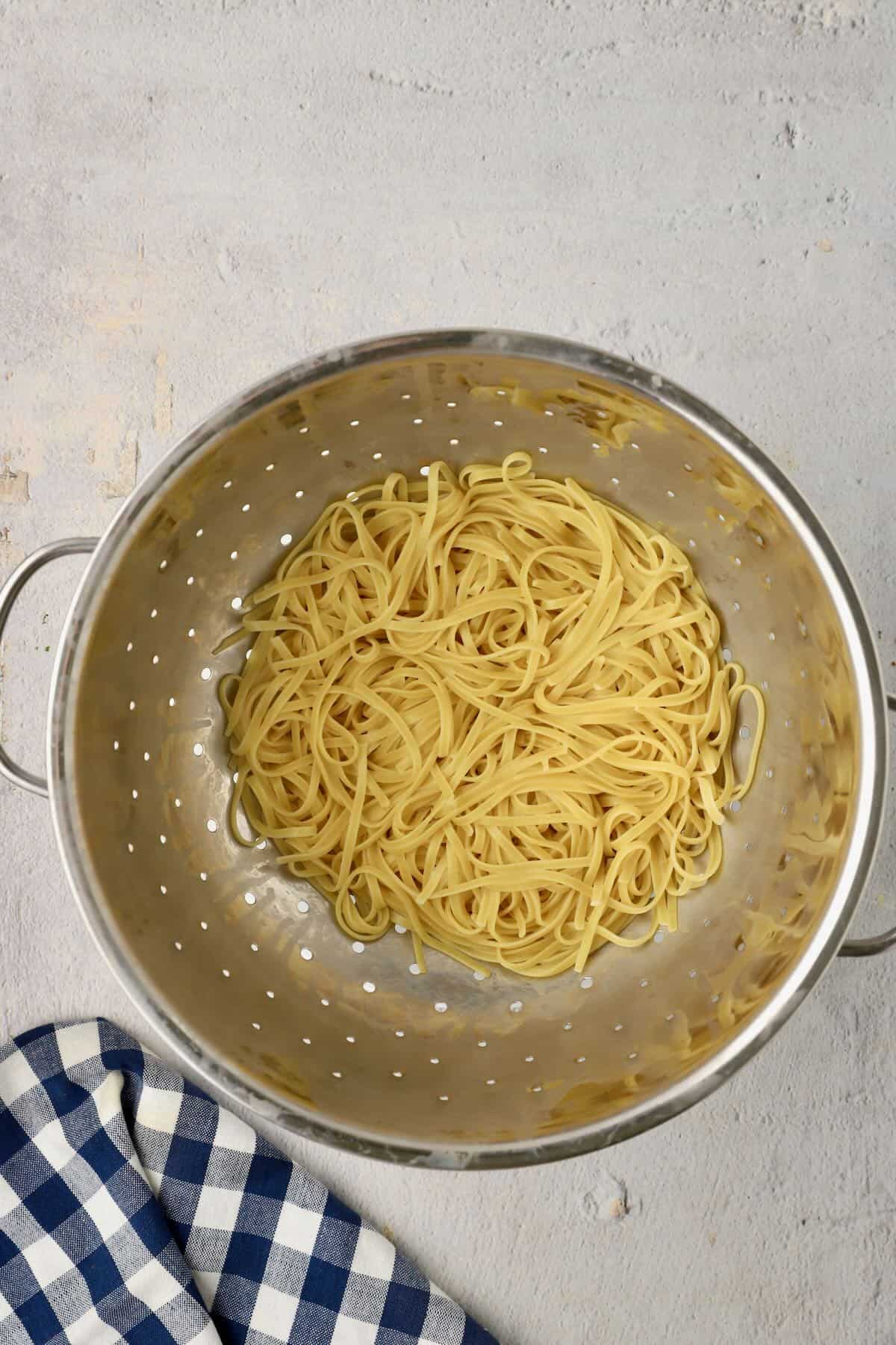 Cooked fettuccine in a colander, draining.