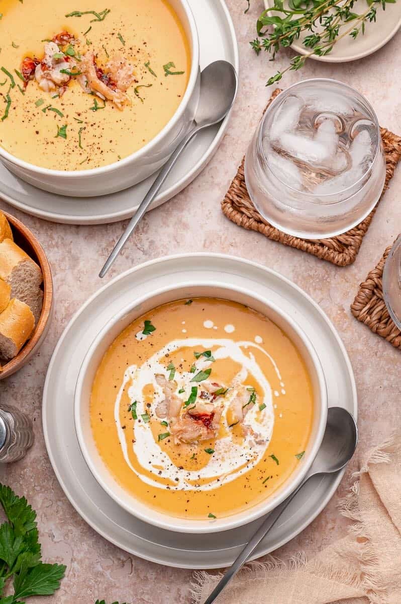 Two bowls of lobster bisque, garnished with lobster meat and herbs, and one has cream added.