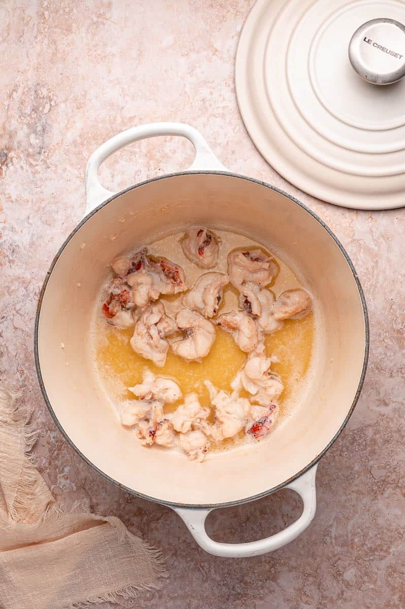 A Dutch oven with lobster meat poaching in garlic butter.