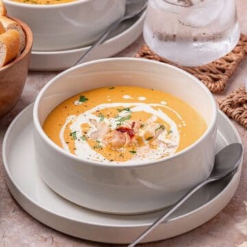 A large bowl full of lobster bisque with chunks of lobster, herbs, and a drizzle of heavy cream.