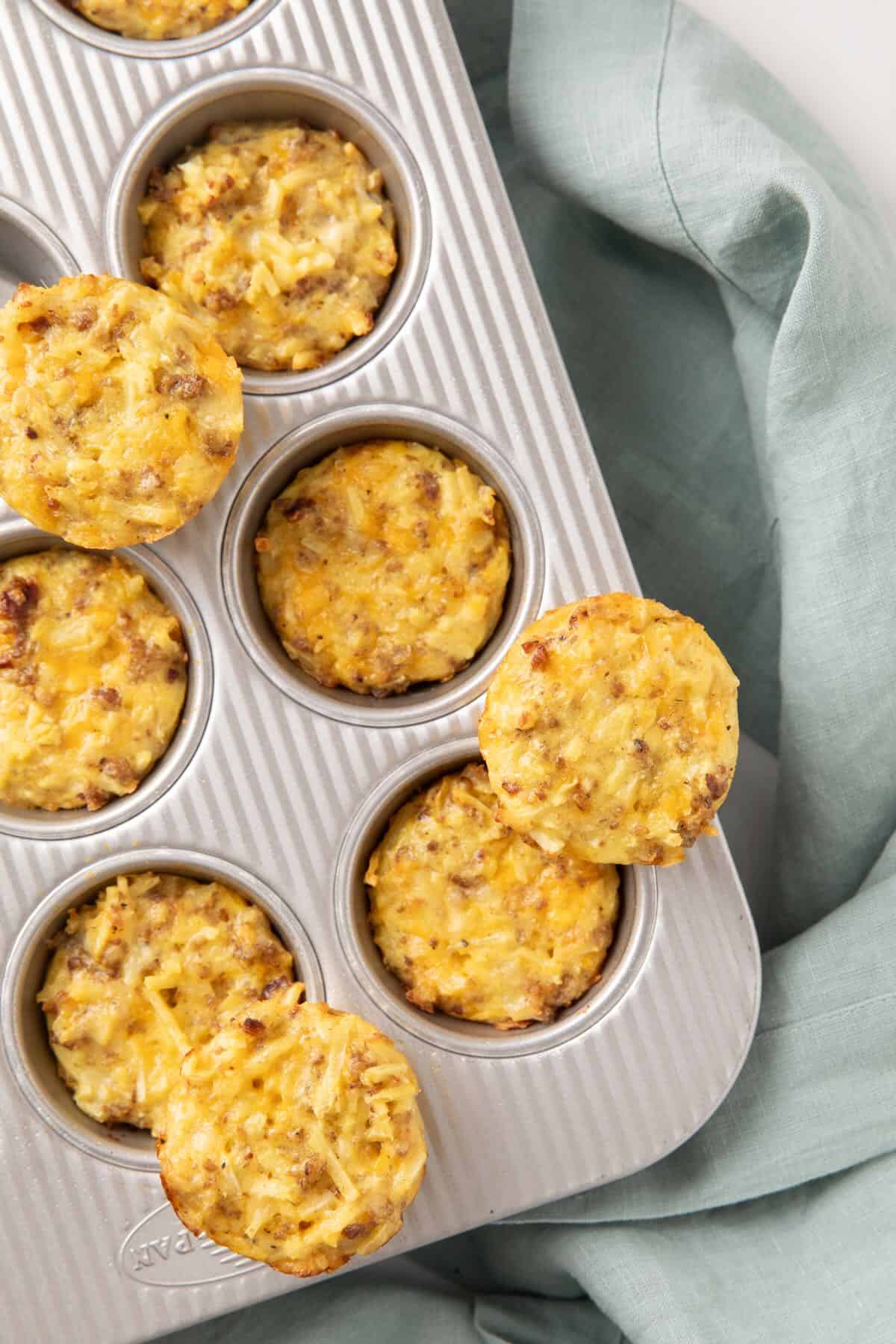 Baked sausage egg bites in a muffin tin, with some sitting on the top.