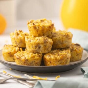 A dozen baked sausage egg bites stacked on a plate with forks and juice.