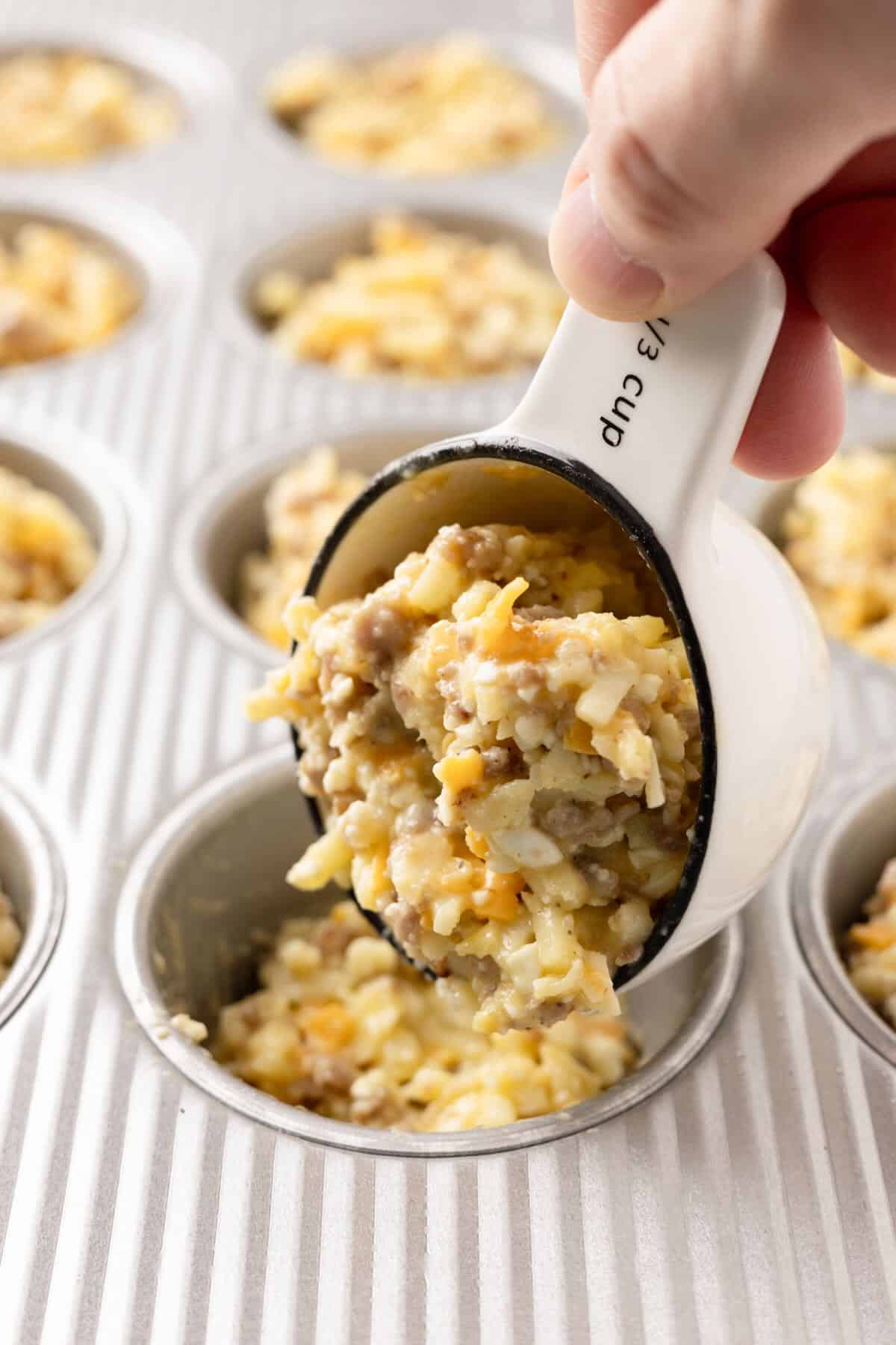 Using a measuring cup to scoop the egg bite mixture into a muffin tin cup.