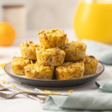 A dozen baked sausage egg bites stacked on a plate with forks and juice.