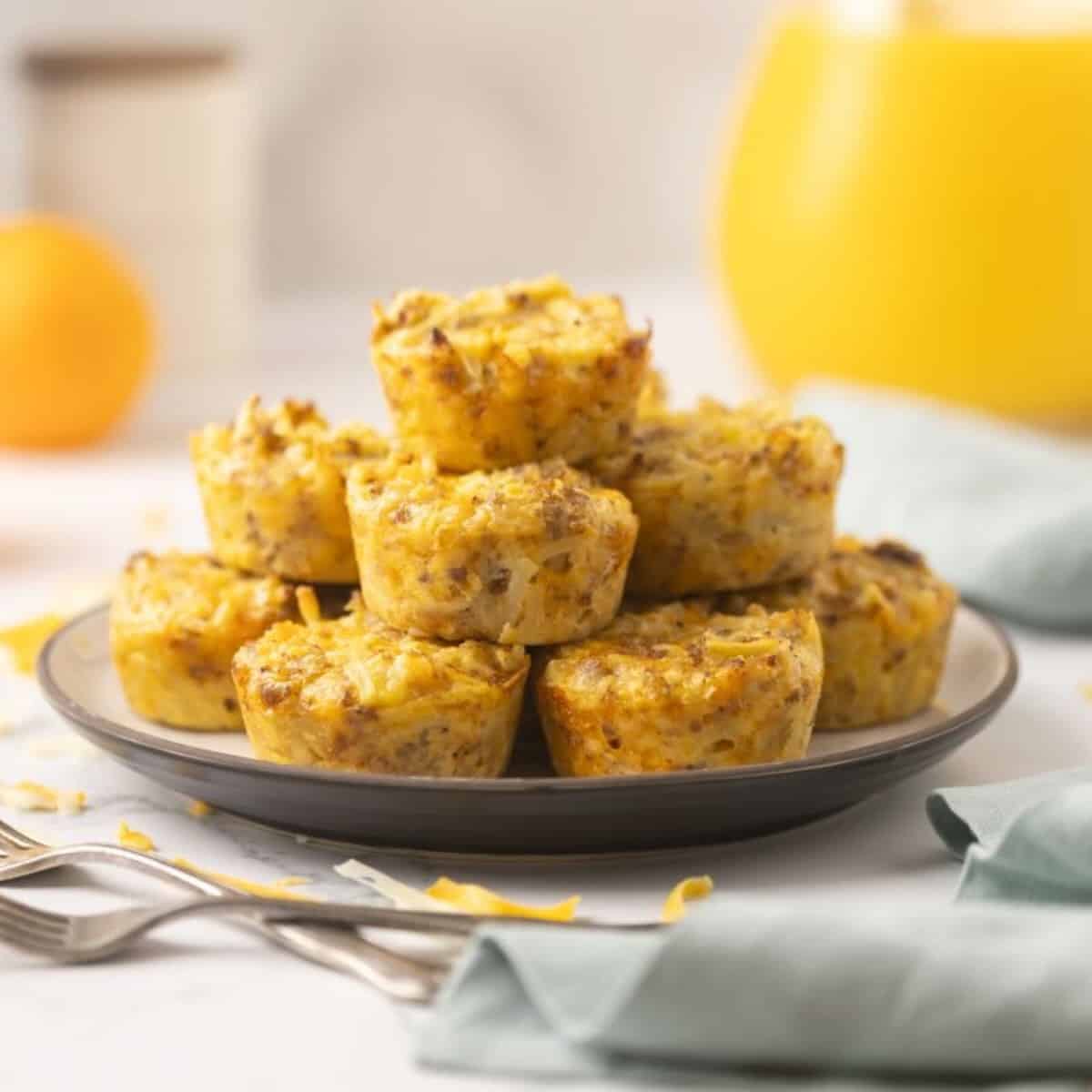 A dozen baked sausage egg bites stacked on a plate with forks and juice.