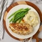 Stuffed chicken breasts on a plate with green beans and mashed potatoes.