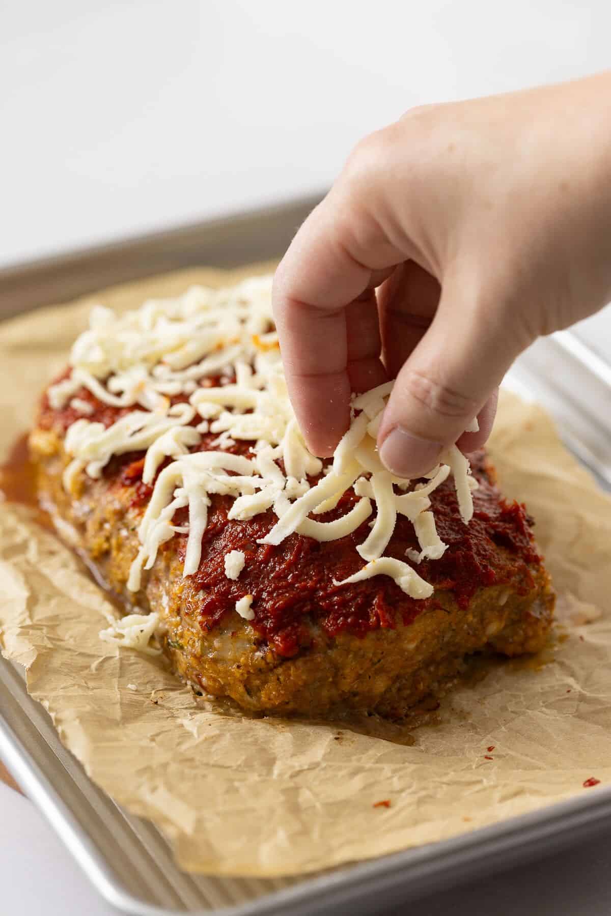 Partially baked meatloaf with glaze and shredded mozzarella added to the top.
