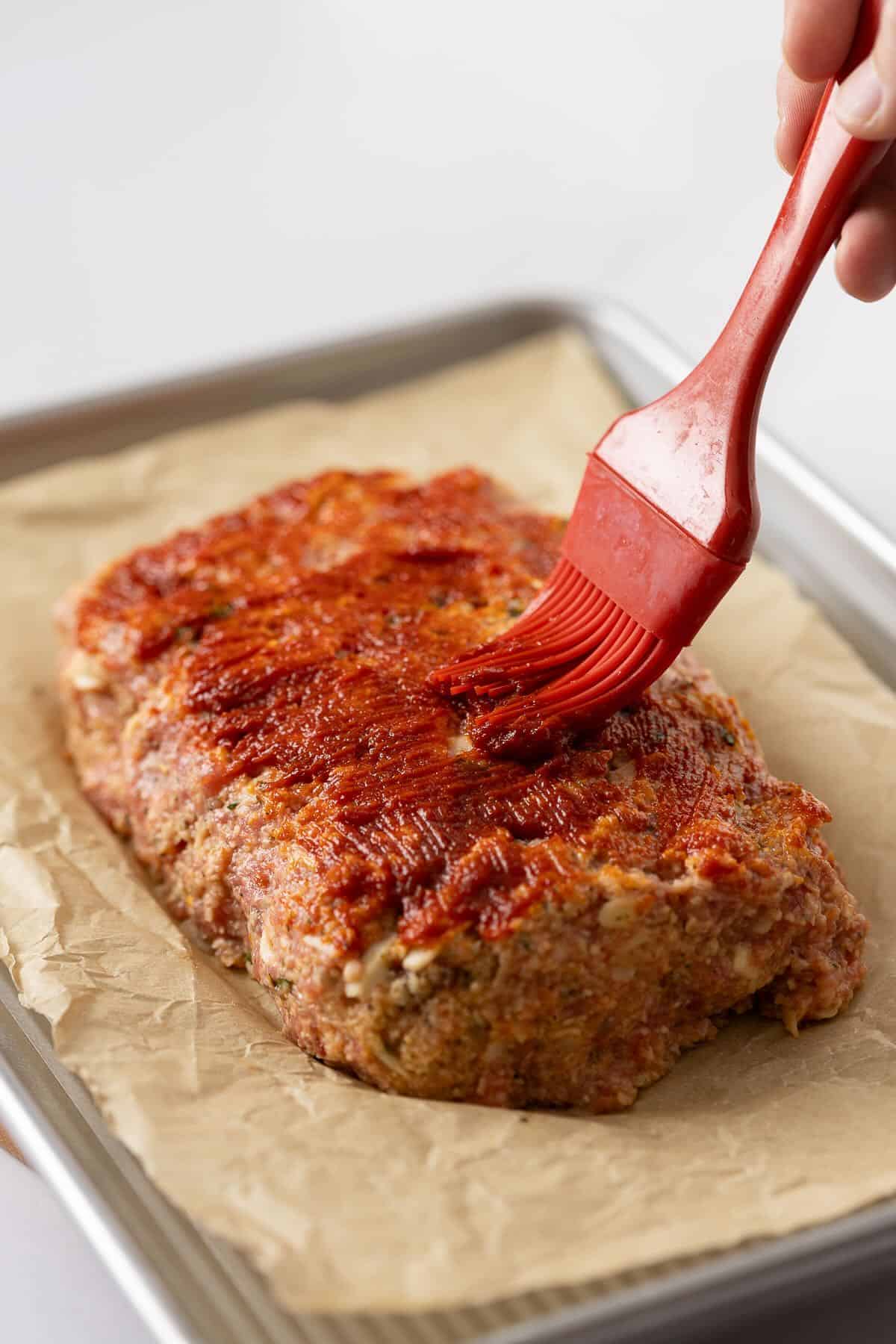 Glaze is brushed on the meatloaf with a pastry brush.