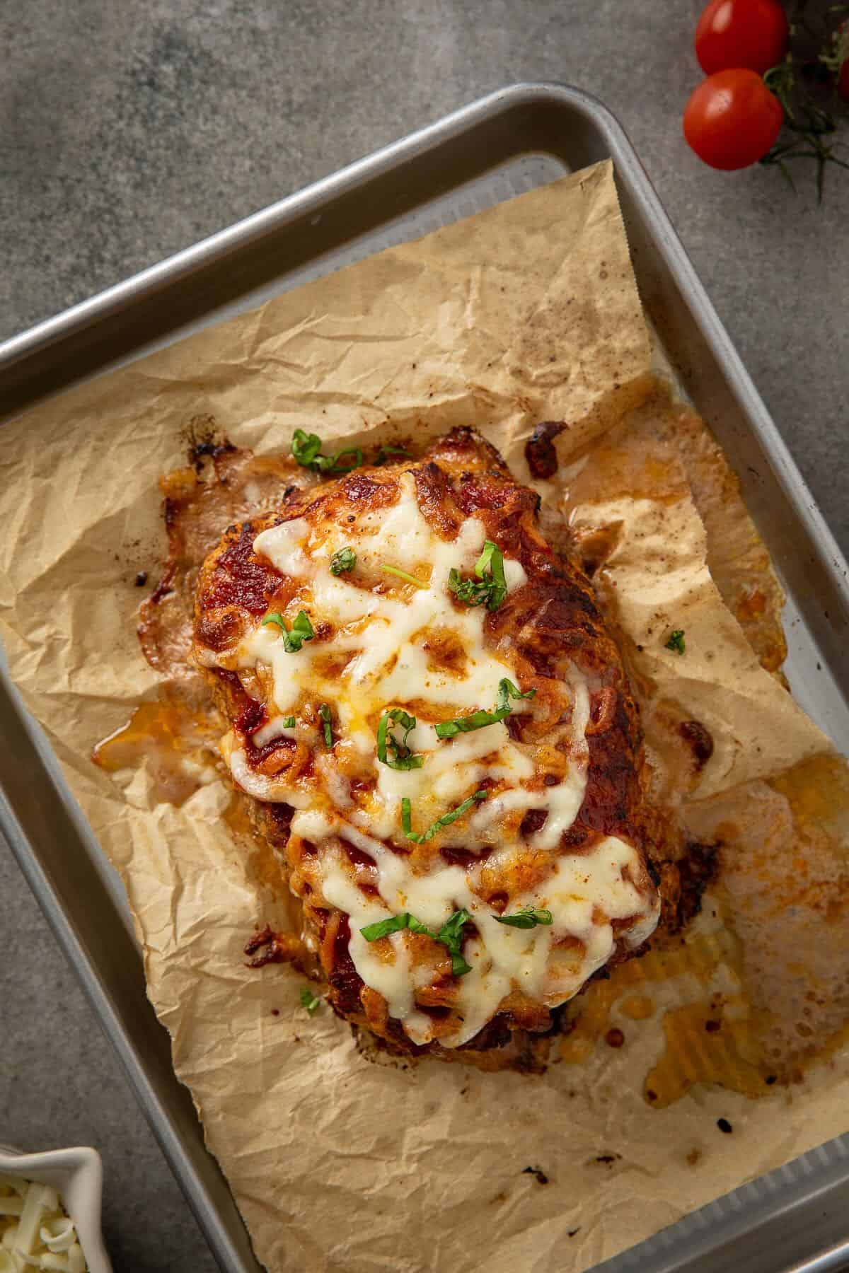 Baked meatloaf on a sheet of parchment topped with glaze and melted cheese.