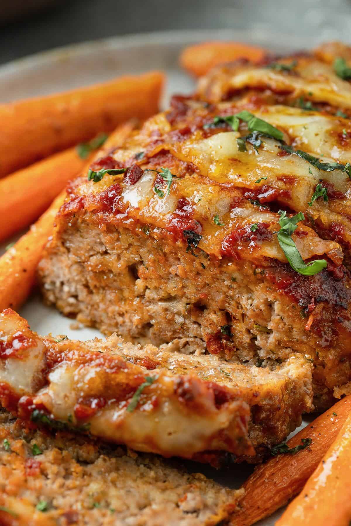 Sliced meatloaf on a cutting board topped with melted cheese and glaze.