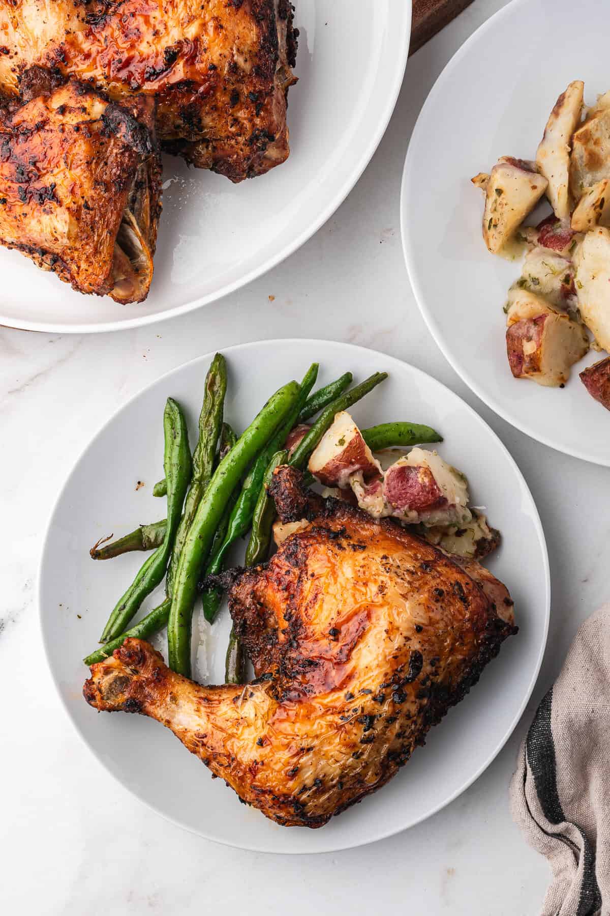 An air fried chicken leg quarter on a plate with green beans and potatoes.