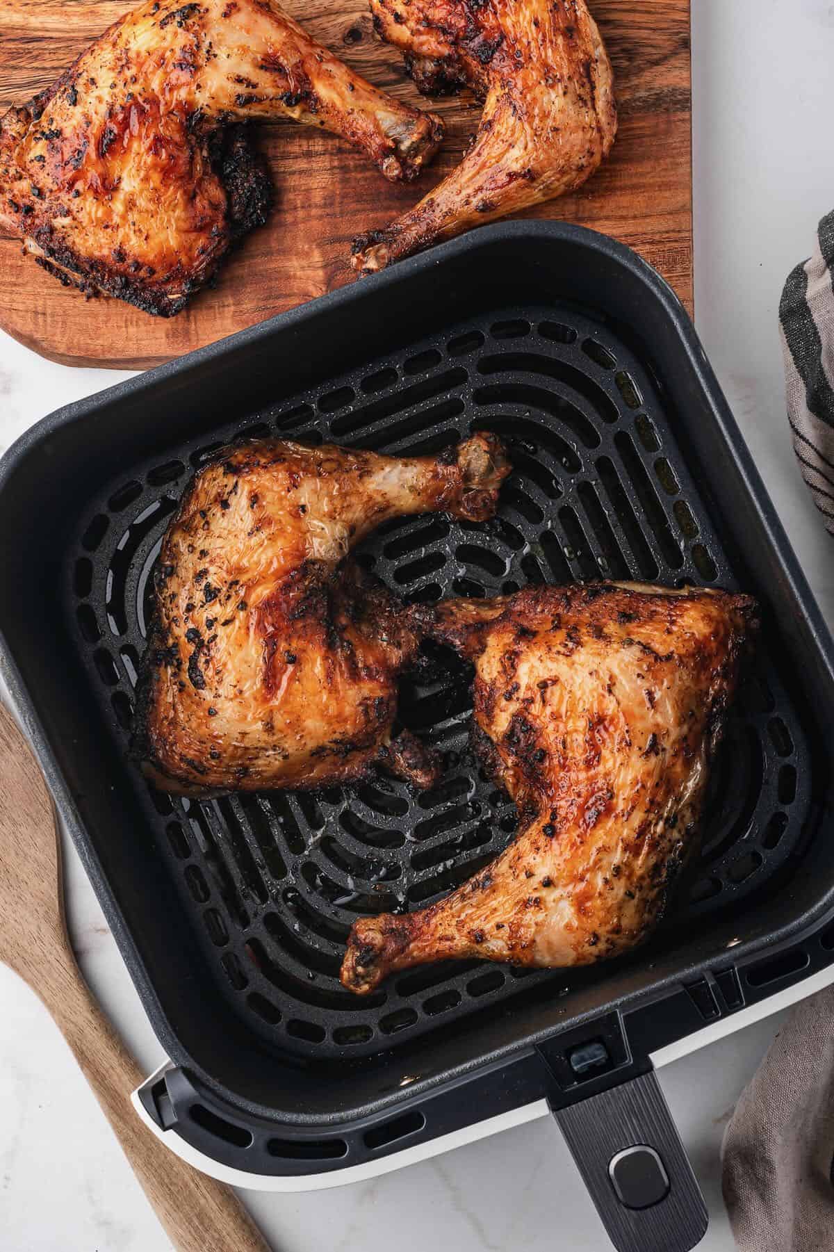 Two air fried chicken leg quarters after air frying in an air fryer basket.