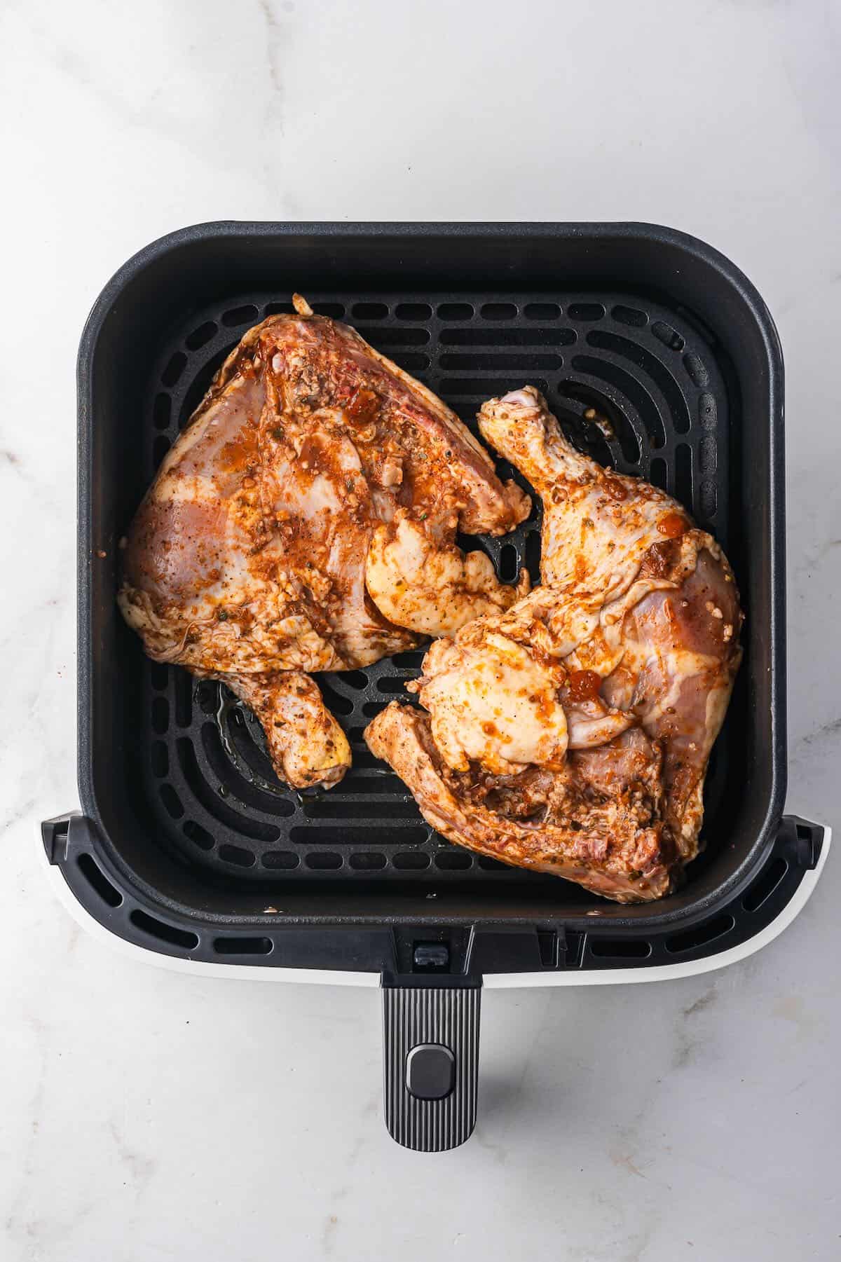 Two chicken leg quarters in an air fryer basket.