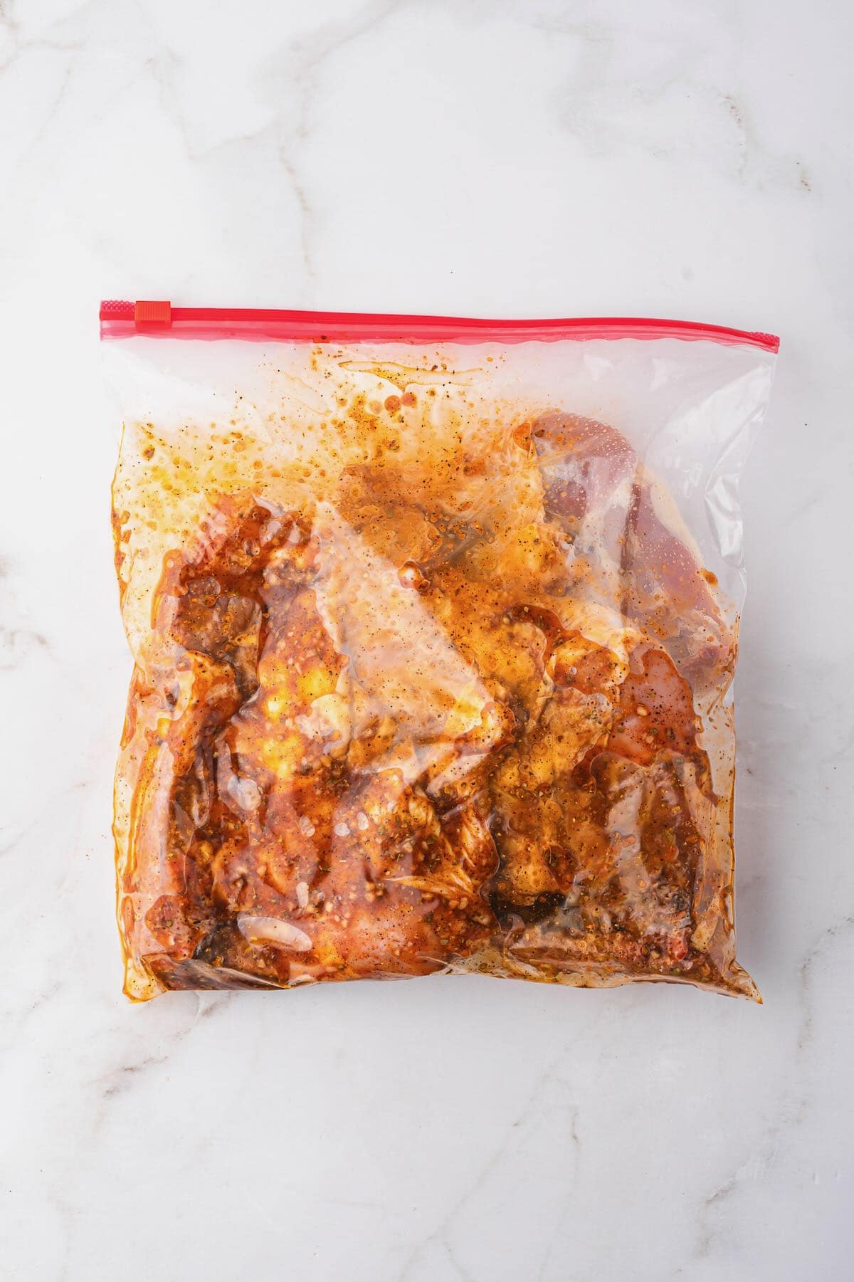 chicken leg quarters marinating in a plastic storage bag with marinade.