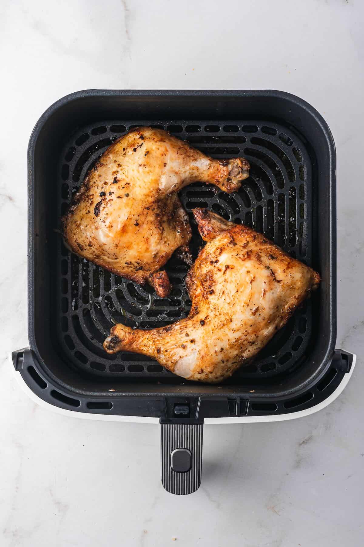 Two chicken leg quarters in the basket of an air fryer after flipping.