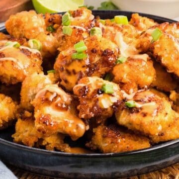 A large serving dish full of fried bang bang chicken, topped with bang bang sauce and chopped scallions.