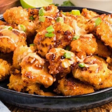 A large serving dish full of fried bang bang chicken, topped with bang bang sauce and chopped scallions.