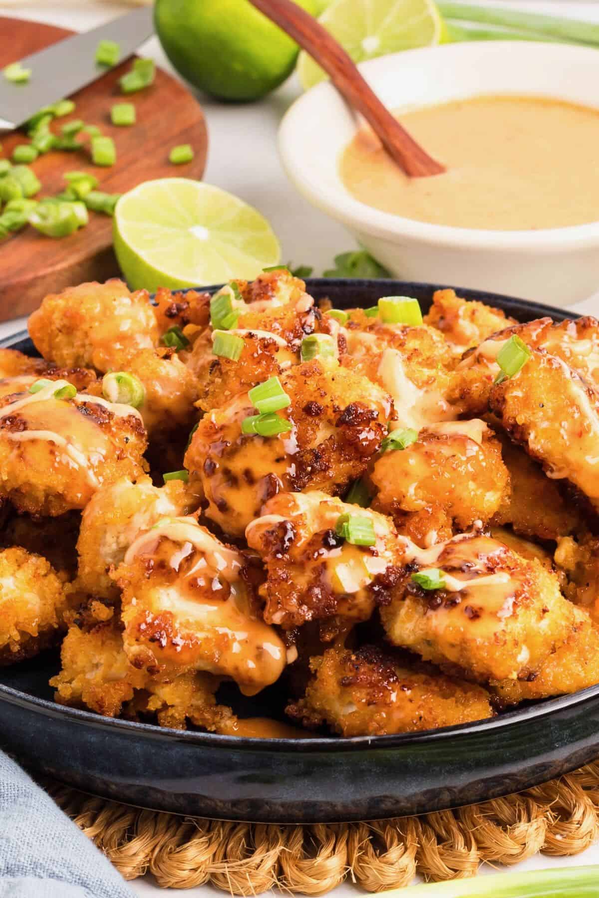 A large serving dish full of bang bang chicken topped with bang bang sauce and chopped scallions.