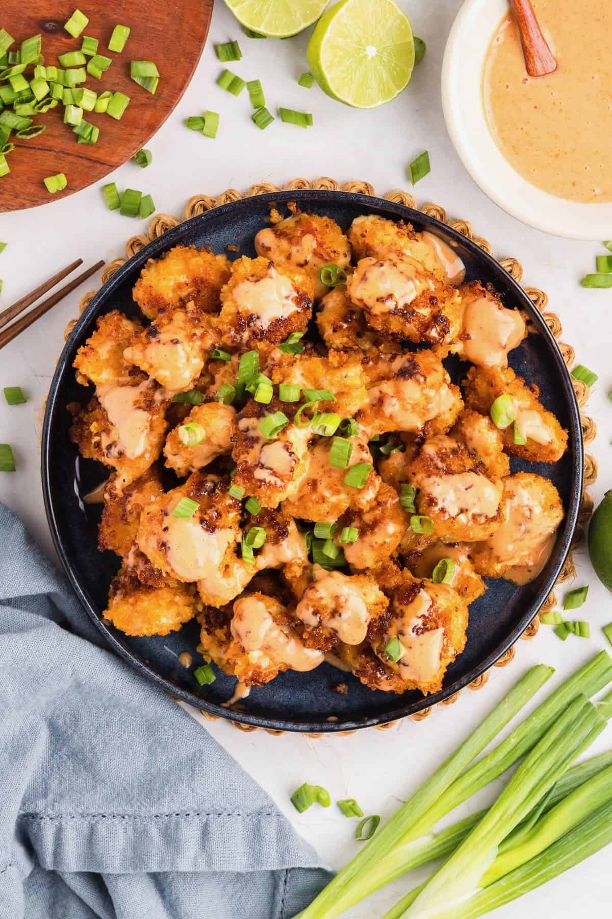 Bang bang chicken in a large black serving dish topped with sauce and chopped green onions.