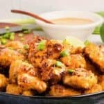 A large serving dish full of bang bang chicken, topped with bang bang sauce, with a bowl of sauce behind it.