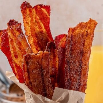 A mason jar full of cooked brown sugar bacon slices on a buffet.