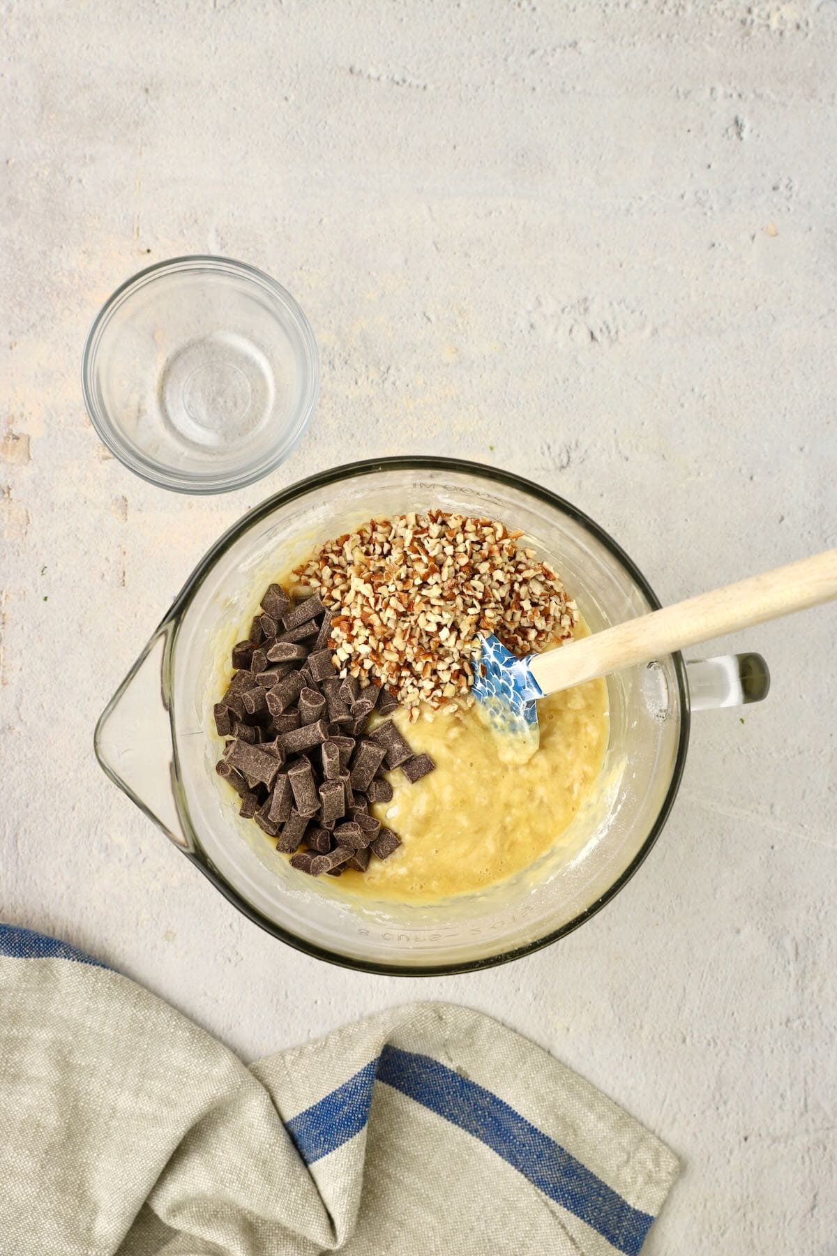 Banana bread batter in a glass bowl with chocolate chunks and pecans added.