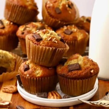 Chocolate chunk Banana muffins stacked on a plate next to a bottle of milk.