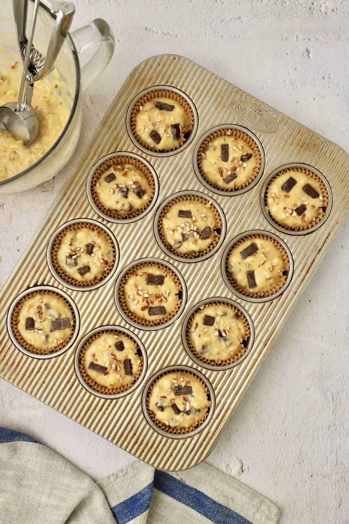 A muffin pan with chocolate chunk banana muffin batter in the cups.