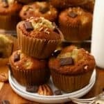 Chocolate chunk banana muffins stacked on a plate, with more muffins behind them.