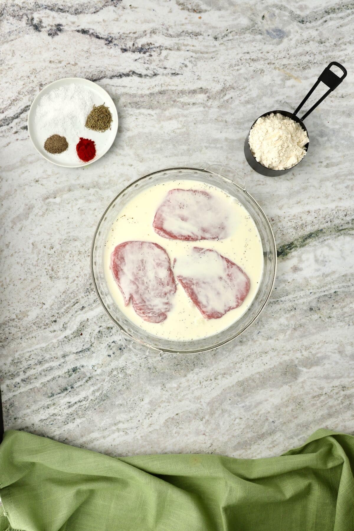 Three steaks marinating in a bowl of buttermilk.