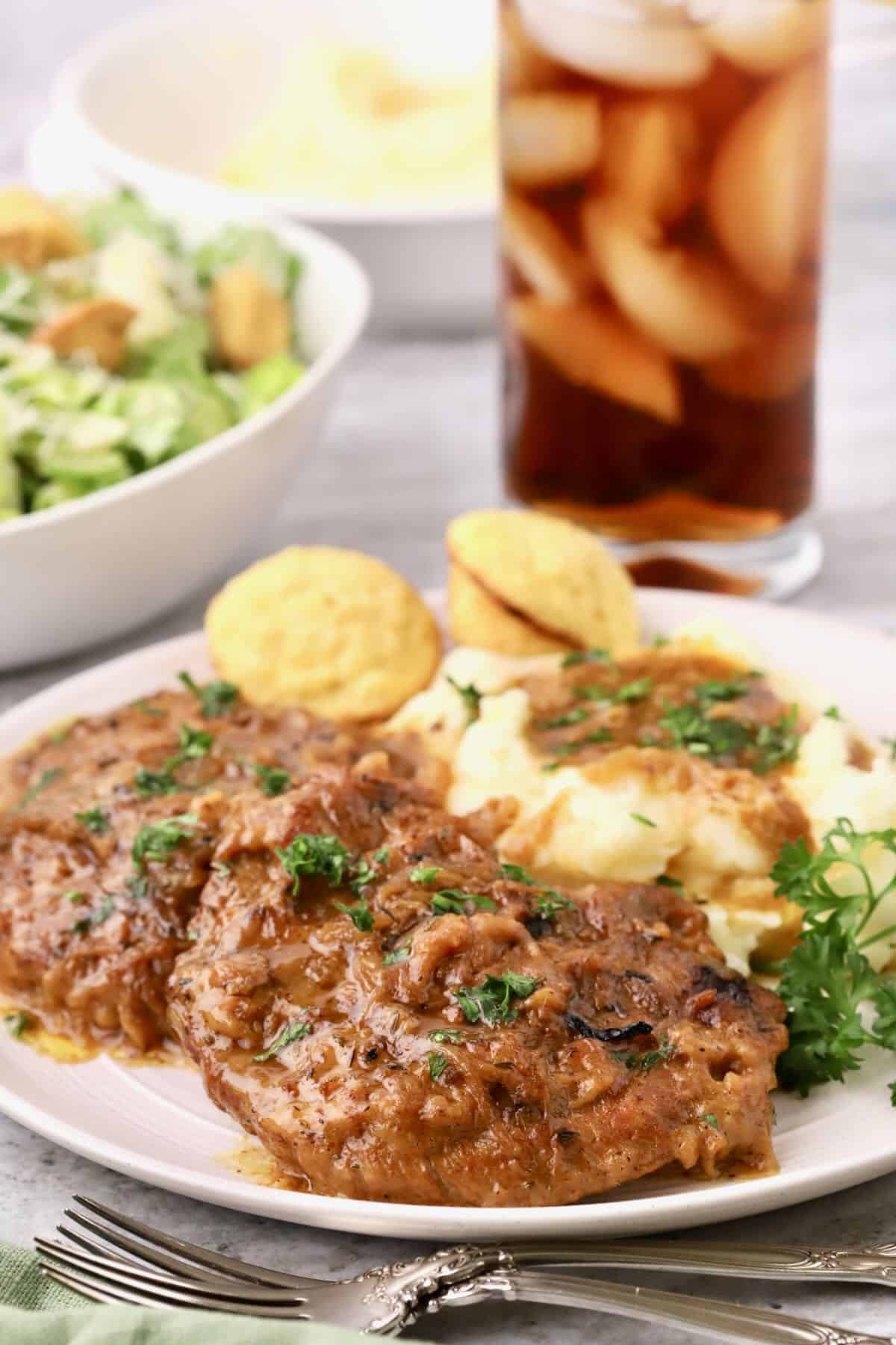 Country style steak covered with onion gravy on a plate with mashed potatoes and mini cornbread muffins.