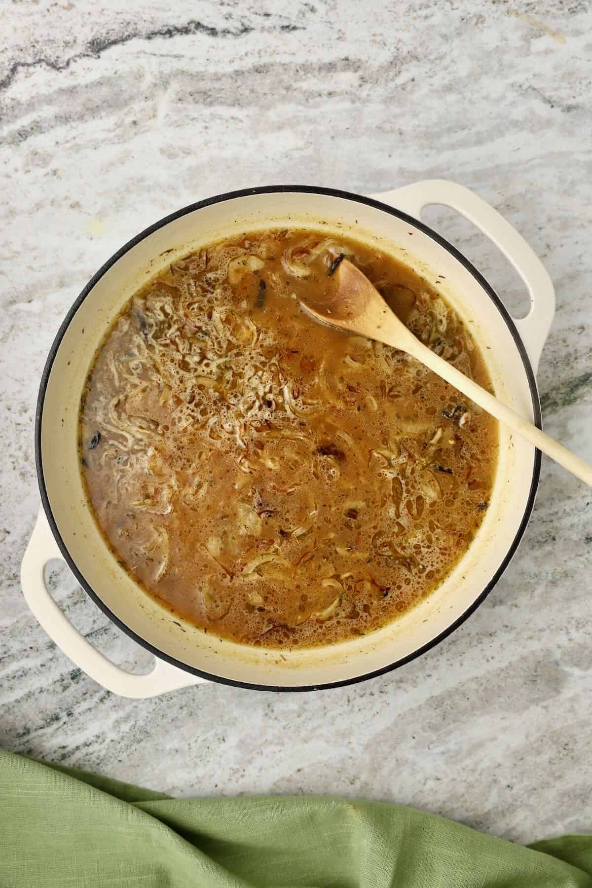 Gravy is cooking in a skillet with a wooden spoon in it.
