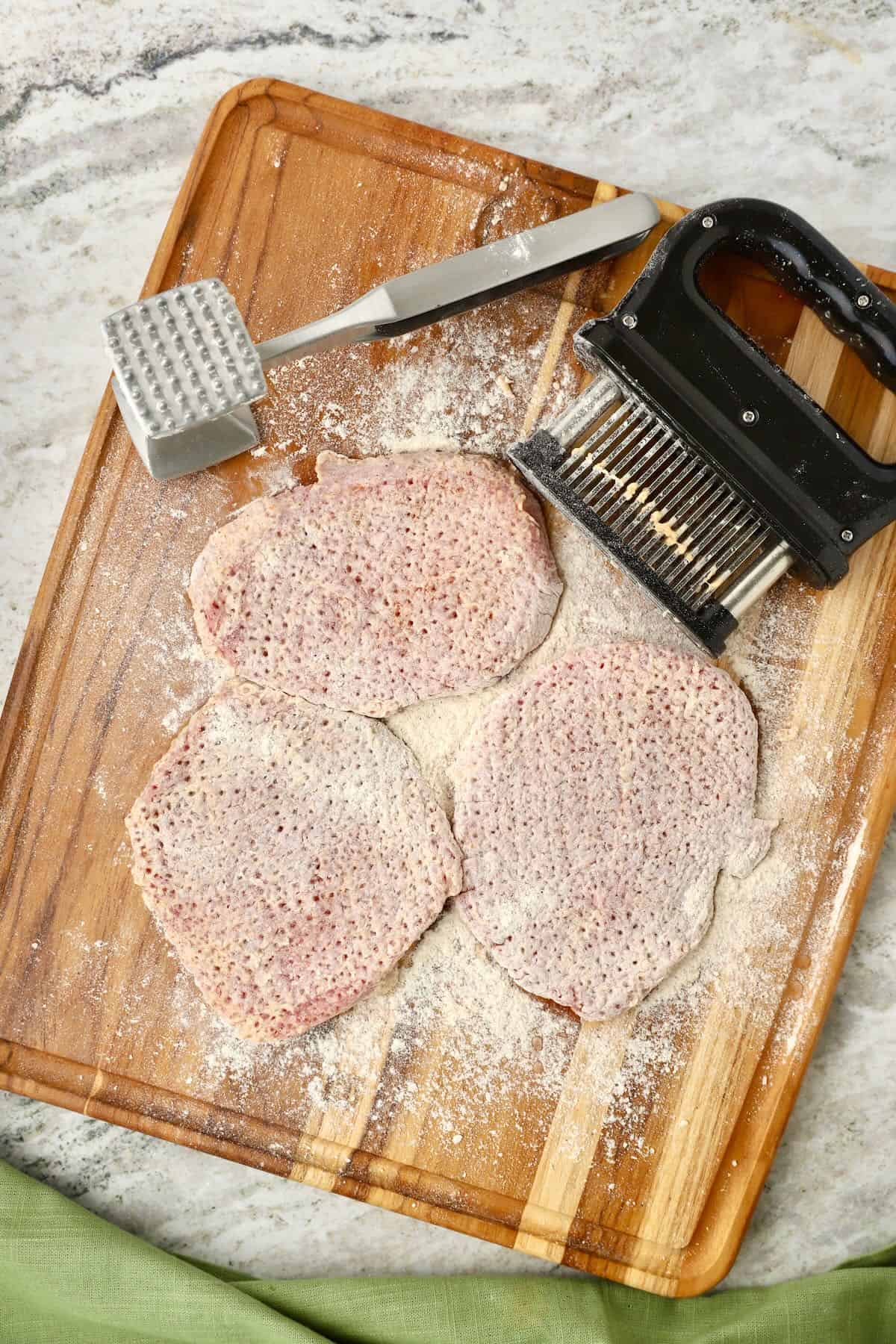 Bottom round steaks covered in flour with a meat mallet that has been used to tenderize them.