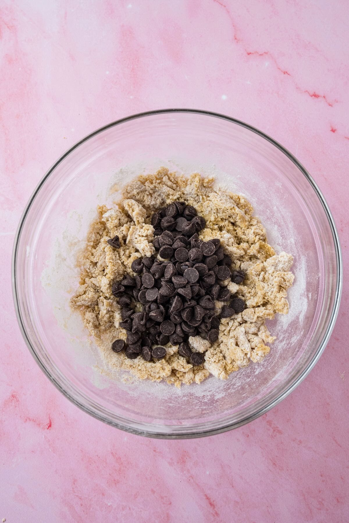 Chocolate chips are added to a bowl full of cookie dough.