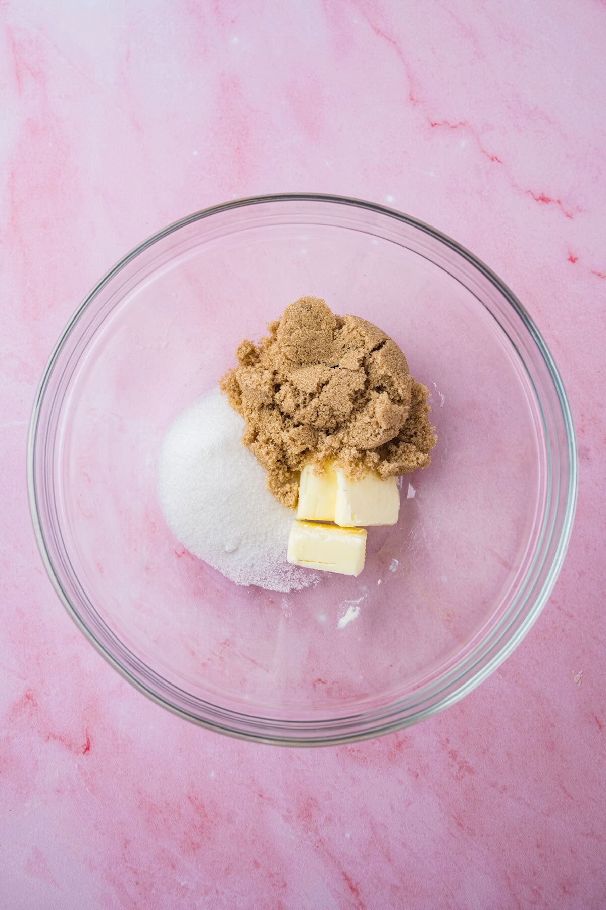 A glass bowl with two types of sugar and butter.