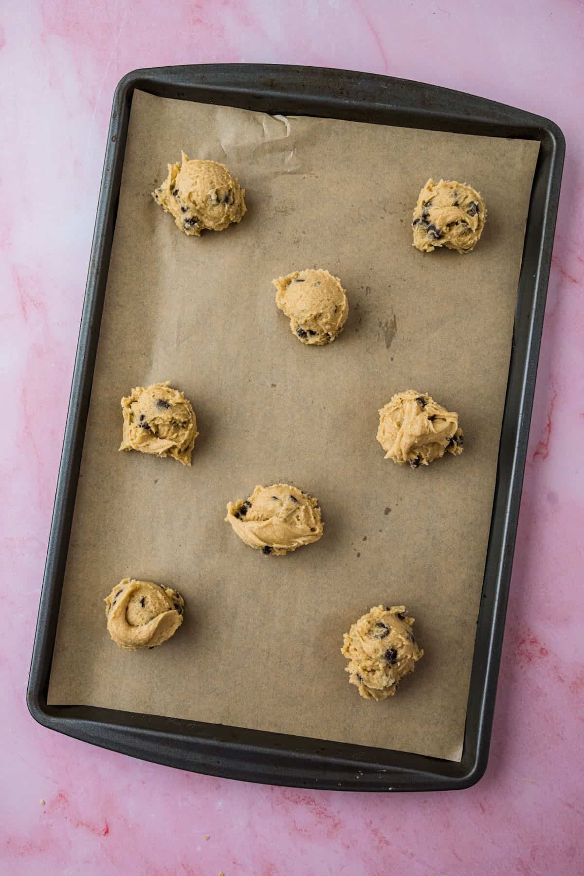 A cookie sheet with balls of chocolate chip cookie dough.