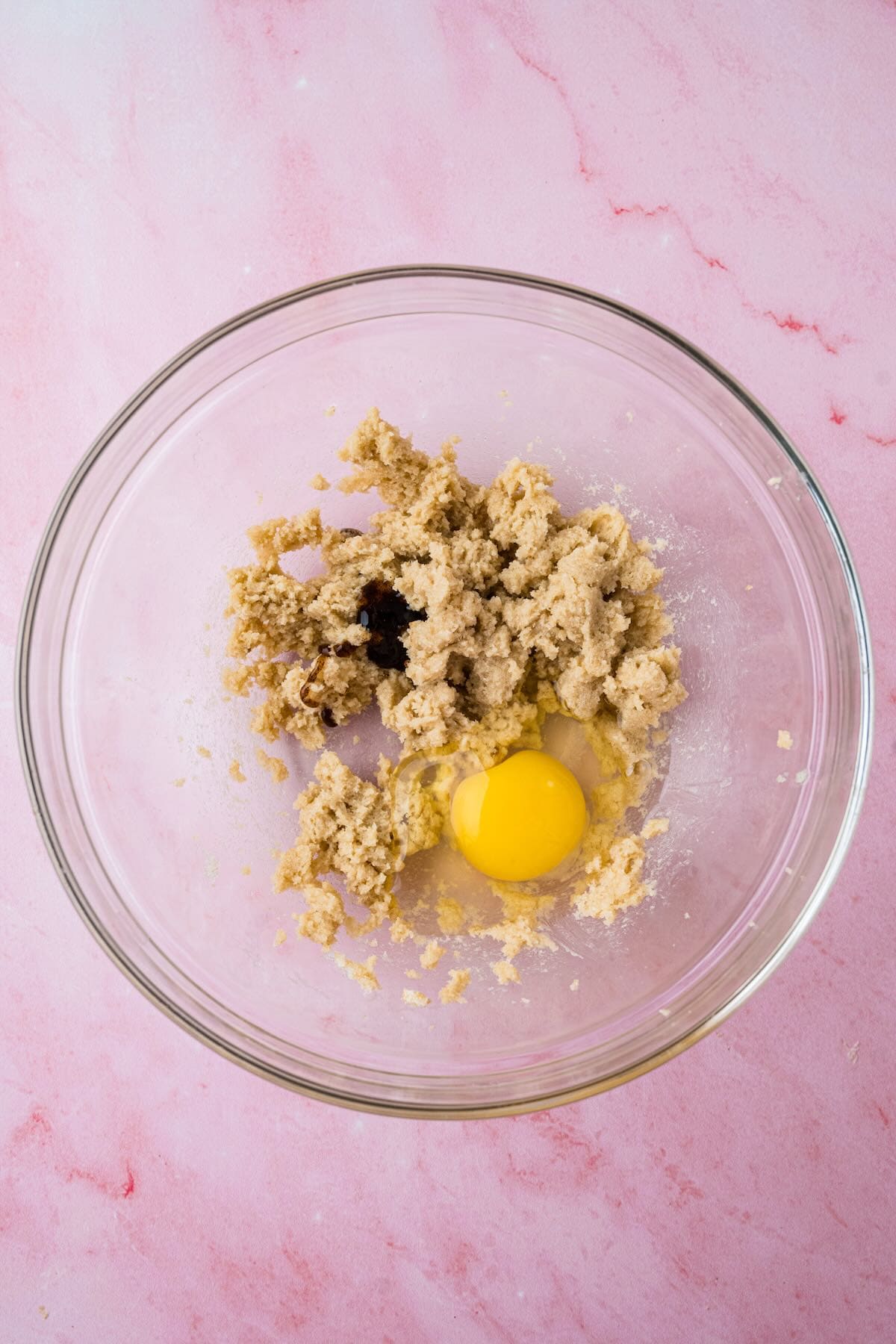 A glass bowl with creamed butter and sugar with an egg yolk added.