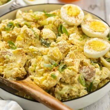 Deviled egg potato salad in a bowl topped with sliced hard boiled eggs, sliced scallions, and paprika.