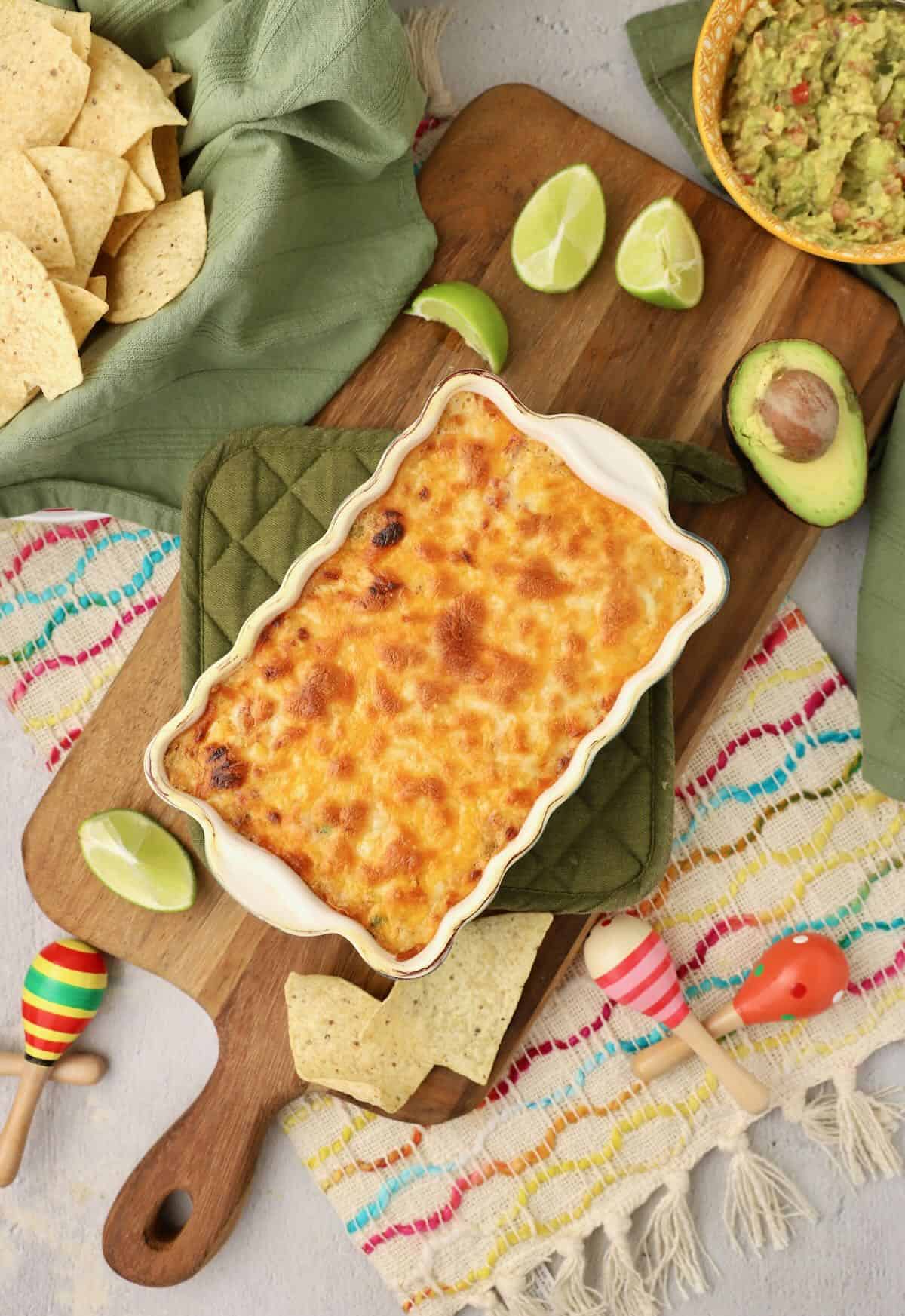 Hot corn dip on a cutting board with lines and avocados.