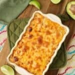 Baked hot corn dip in a dish topped with melted cheese on a cutting board.