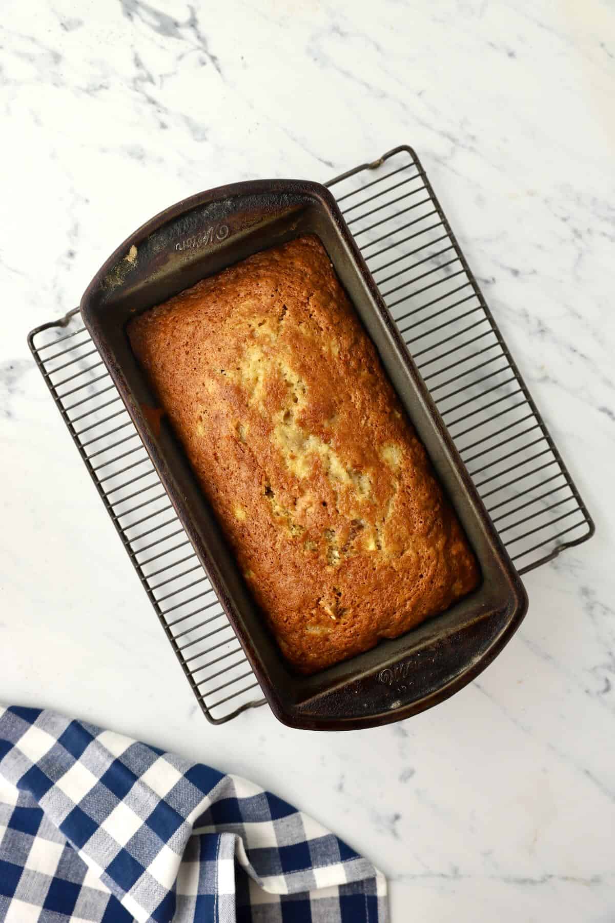 Baked peach bread in a loaf pan, cooling on a wire rack.