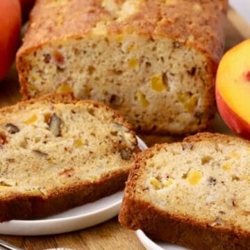 A loaf of freshly baked peach bread on a cutting board with slices cut on plates.