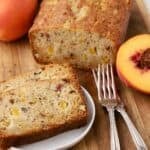 A loaf of freshly baked peach bread on a cutting board with slices cut on a plate.