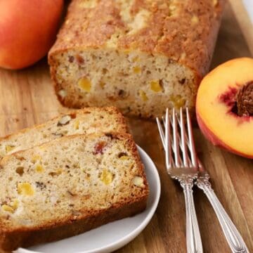 A loaf of freshly baked peach bread on a cutting board with slices cut on a plate.