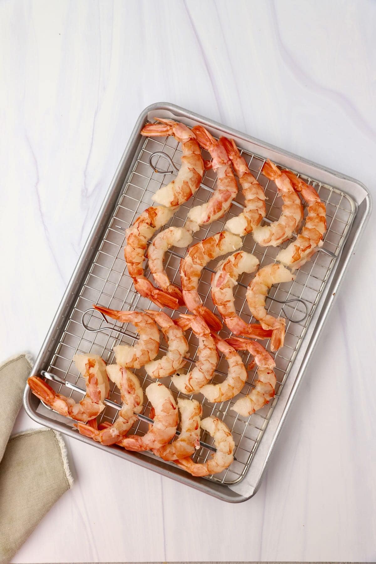 Four metal skewers with raw royal red shrimp threaded on them.