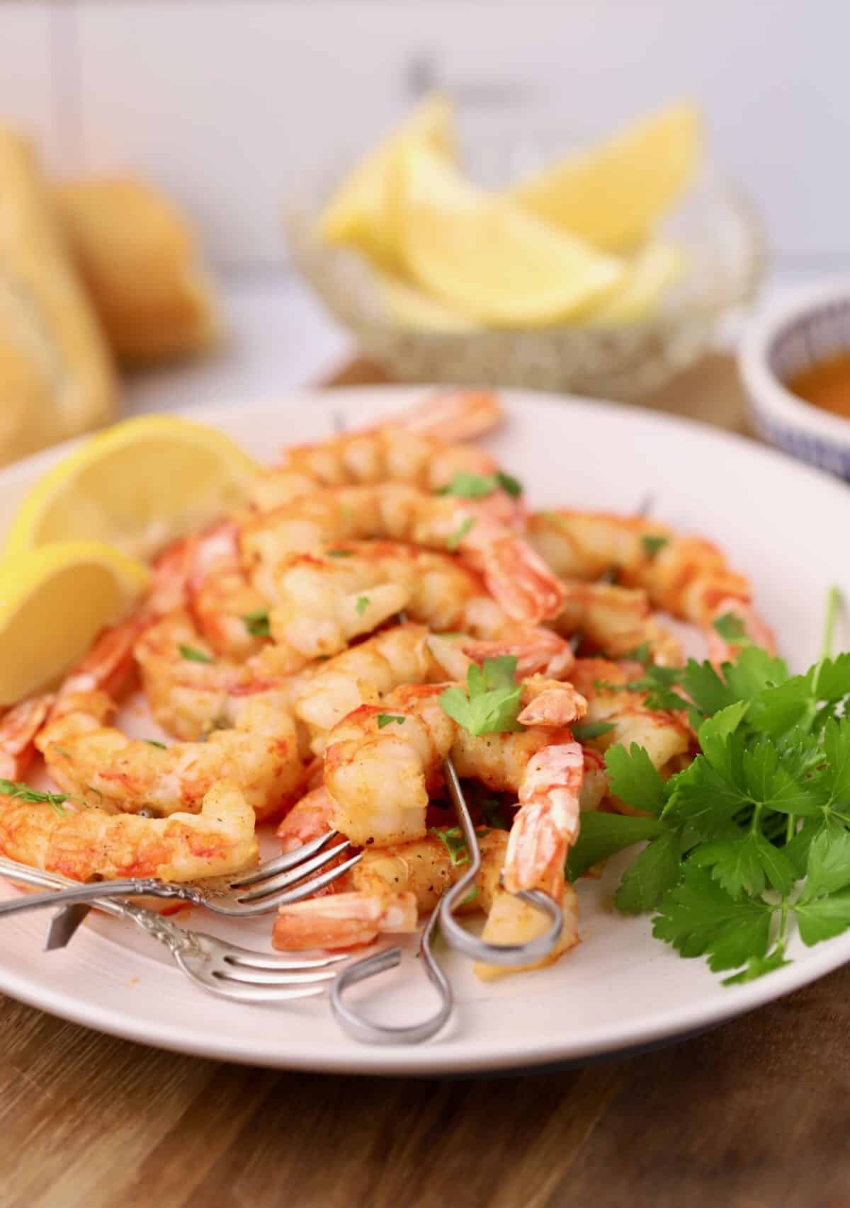 Oven-roasted shrimp on skewers on a serving plate garnished with parsley and sliced lemons.