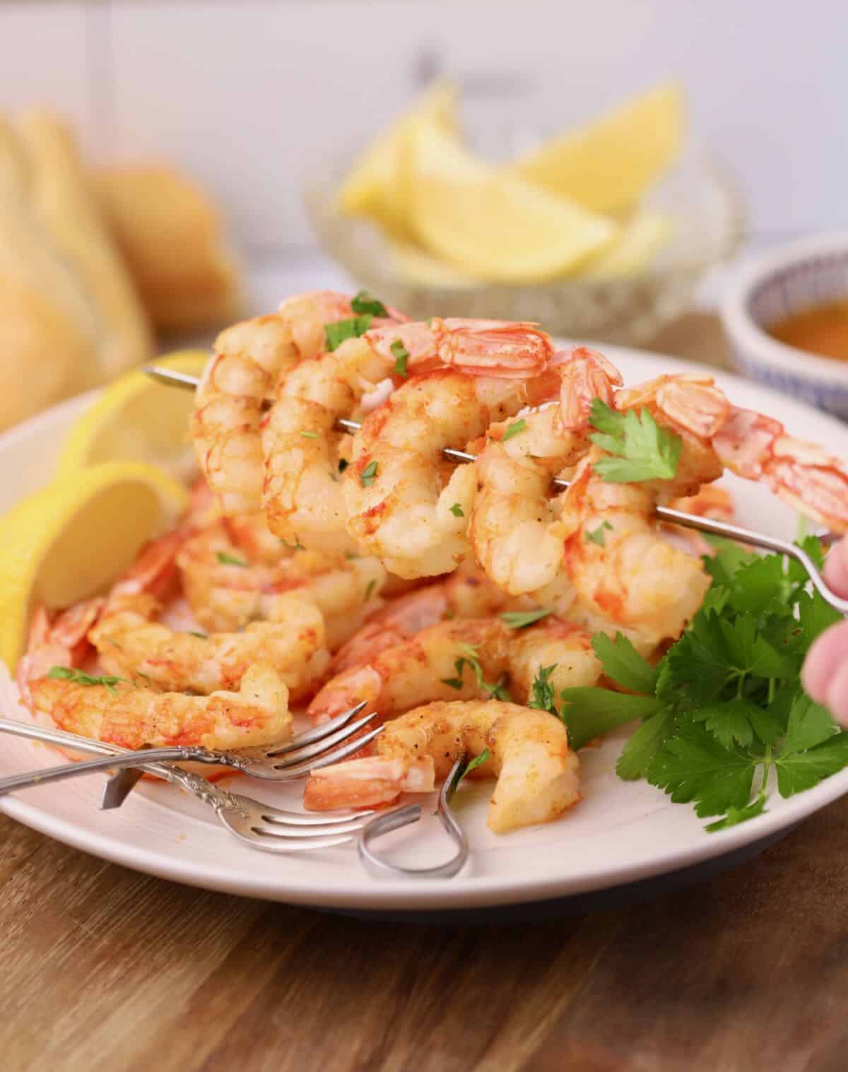 Oven roasted shrimp on skewers on a white plate, garnished with parsley.