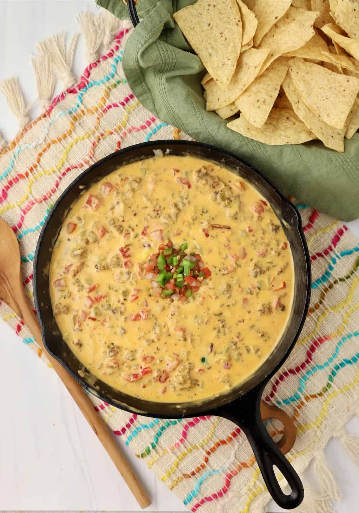 Smoked queso dip in a cast iron skillet next to a basket of tortilla chips.