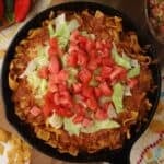 Walking Taco Casserole in a cast iron skillet topped with lettuce and tomatoes.