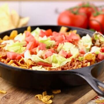 Walking Taco Casserole in a cast iron skillet topped with lettuce and tomatoes.